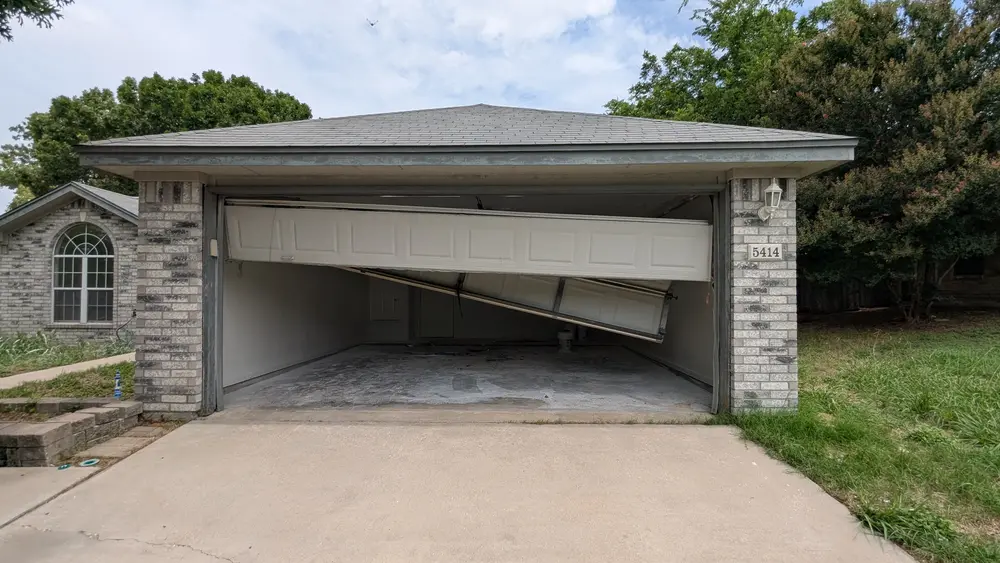 A garage door that has come off its track and is hanging open